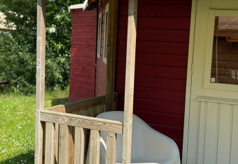 En solbeskinnet veranda med hvid stol foran en rød træhytte ved Zweedse Huisjes i Beloofde Land.