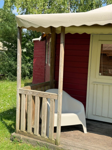 Porche soleado con una silla blanca frente a una cabaña roja en Zweedse Huisjes, Beloofde Land, Países Bajos.
