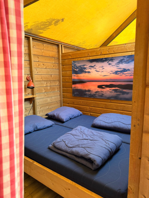 Vue intérieure d’une cabane en bois avec lit double et literie bleue chez Zweedse Huisjes au Beloofde Land.