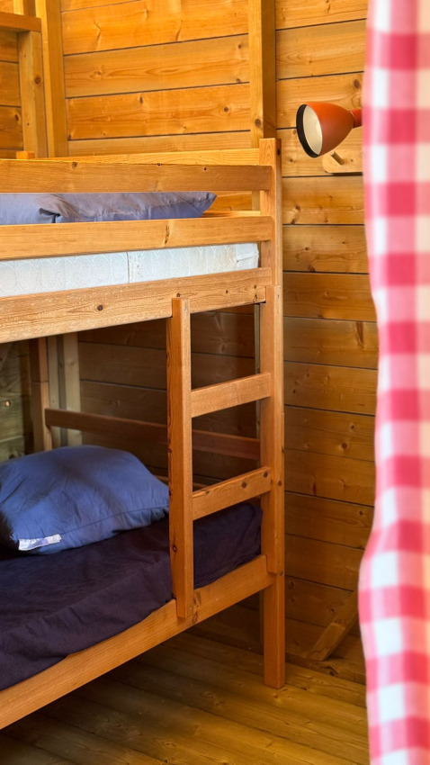 Holzhütte mit Etagenbett, blauer Bettwäsche und rot-weiß kariertem Vorhang in Zweedse Huisjes, Beloofde Land, Niederlande.