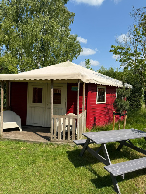 Red lodge with porch at Zweedse Huisjes, Beloofde Land, Netherlands, with lawn and picnic table outside.