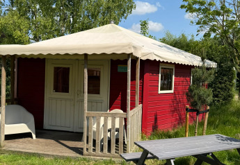 Red lodge with porch at Zweedse Huisjes, Beloofde Land, Netherlands, with lawn and picnic table outside.