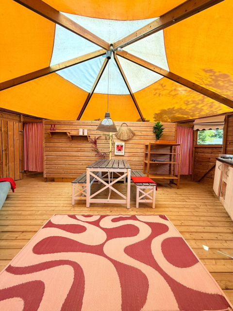 Interior de lodge acogedor con paredes de madera, toldo colorido y mesa de comedor en Beloofde Land, Países Bajos.