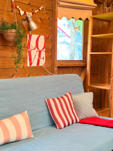 Intérieur douillet d’un lodge aux Zweedse Huisjes, canapé bleu, coussins rayés et affiche LOVE sur le mur.