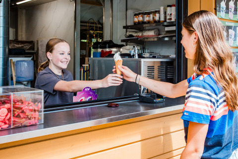 Two young girls exchange an ice cream cone at a kiosk in Safaritent basic, Beloofde Land, Netherlands.