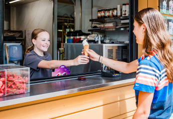 Twee jonge meisjes geven een ijsje aan elkaar bij de kiosk in Safaritent basic, Beloofde Land, Nederland.