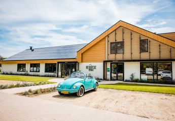 A blue vintage car in front of Safaritent basic at Beloofde Land in the Netherlands, on a bright sunny day.
