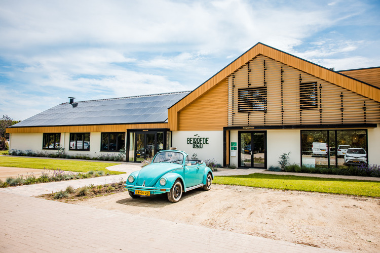 Coche clásico azul frente a Safaritent basic en Beloofde Land, Países Bajos, bajo un cielo soleado y despejado.