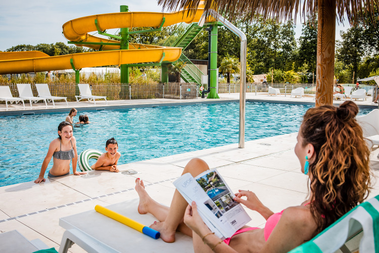 Mutter entspannt am Pool, während Kinder im Wasser spielen, bei Safaritent basic im Beloofde Land, Niederlande.