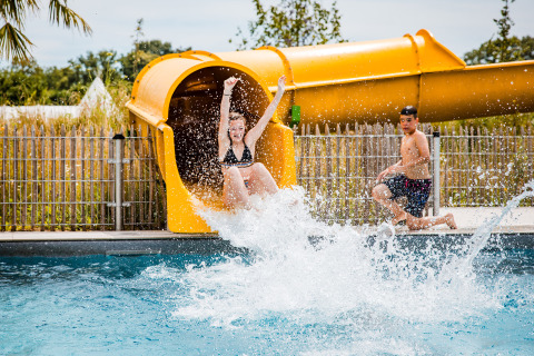 Kids playing in a pool with a yellow water slide at Safaritent basic at Beloofde Land, Netherlands.