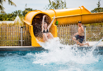 Kinderen spelen in het zwembad met een gele glijbaan bij Safaritent basic op Beloofde Land, Nederland.