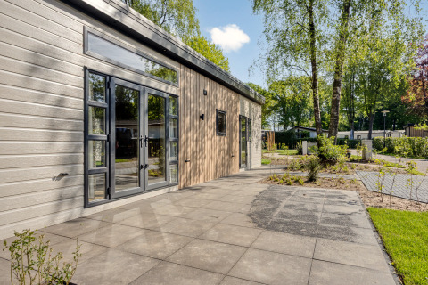 Modern Nova 4 person lodge at Bospark Ede, Netherlands, with patio and trees in a peaceful green setting.