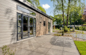 Moderne lodge Nova 4 personen bij Bospark Ede in Nederland, met terras en uitzicht op bomen en groen.