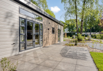 Modern Nova 4 person lodge at Bospark Ede, Netherlands, with patio and trees in a peaceful green setting.