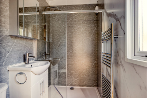 Salle de bain moderne dans un lodge avec douche en verre, lavabo blanc, miroir et sèche-serviettes.