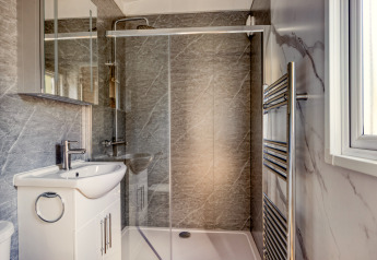 Baño moderno en una cabaña con ducha de vidrio, lavabo blanco, espejo y radiador toallero cromado.