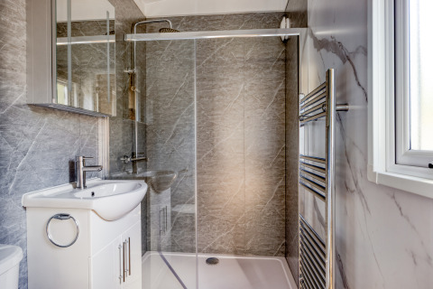 Moderne lodgebadkamer met glazen douchecabine, wit wastafelmeubel, spiegel en handdoekradiator.