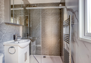 Modern lodge bathroom with glass shower enclosure, white basin unit, mirror cabinet, and towel radiator.