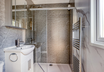 Modern lodge bathroom with glass shower enclosure, white basin unit, mirror cabinet, and towel radiator.
