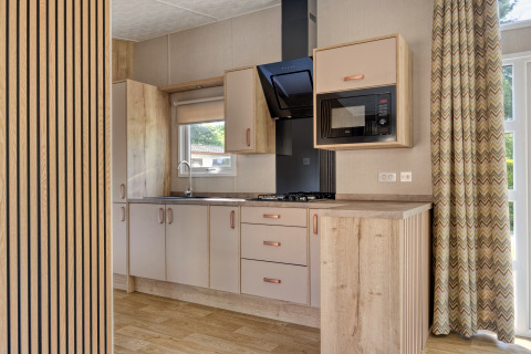 Modern lodge kitchenette with wooden cabinets, gas hob, microwave, and large windows with curtains.