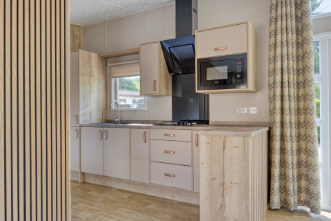 Moderne Lodge-Küche mit Holzschränken, Gasherd, Mikrowelle und großen Fenstern mit Vorhängen.