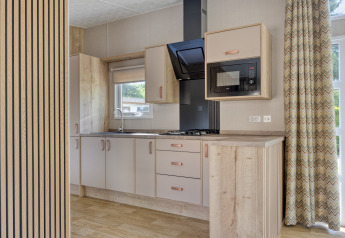 Modern lodge kitchenette with wooden cabinets, gas hob, microwave, and large windows with curtains.