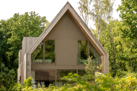 Zeitgemäße Lodge mit Satteldach und großen Fenstern, umgeben von Bäumen, bei Woodz Lodges, Belgien.