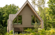 Moderne lodge med stort skråt tag og store vinduer omgivet af grøn natur ved Woodz Lodges, Belgien.