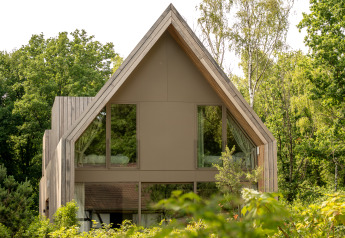 Zeitgemäße Lodge mit Satteldach und großen Fenstern, umgeben von Bäumen, bei Woodz Lodges, Belgien.