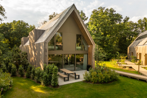 Moderne lodge met hoge ramen en terras, omringd door een groene tuin en bomen aan een lodge.