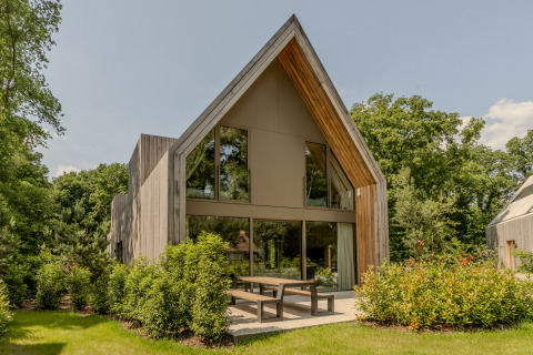 Lodge moderno con amplios ventanales de vidrio y fachada de madera, rodeado de vegetación y árboles en un día soleado.