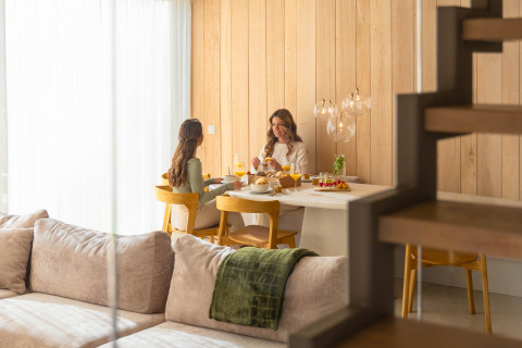 Deux femmes savourent un petit déjeuner à une table en bois dans un lodge moderne et chaleureux.