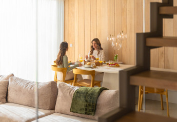 Due donne fanno colazione insieme a un tavolo di legno in un accogliente lodge moderno e luminoso.