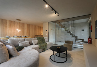 Sala moderna y espaciosa en Group Lodge en Woodz Lodges, Bélgica, con paneles de madera y escalera de vidrio.