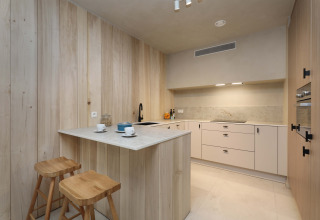 Cocina moderna con paneles de madera clara y taburetes en Group Lodge de Woodz Lodges en Bélgica.