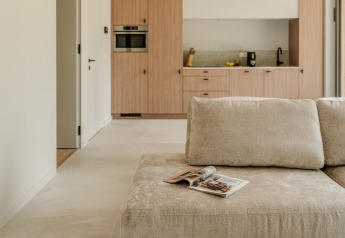 Salon moderne avec canapé beige, magazine et vue sur la cuisine à Group Lodge, Woodz Lodges, Belgique.