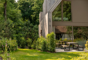 Lodge moderno con grandi finestre e area esterna con panchine, immerso nel verde della foresta.