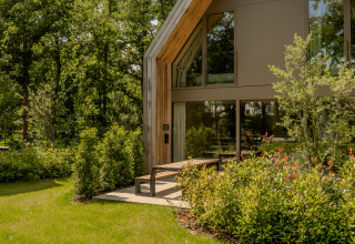 Lodge moderno con ventanas grandes, rodeado de vegetación exuberante y árboles en un entorno natural tranquilo.