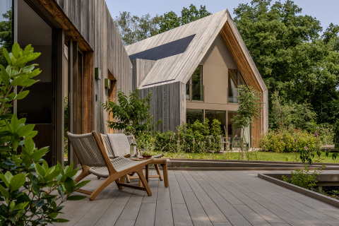 Moderne træhytte med store vinduer og terrasse, omgivet af grønne træer ved Group Lodge, Woodz Lodges, Belgien.