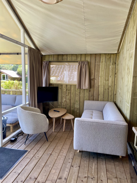 Binnenkant van de Luna Lodge safaritent op Camping de Noetselerberg met bank, stoel en tafel.