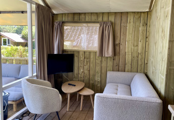 Binnenkant van de Luna Lodge safaritent op Camping de Noetselerberg met bank, stoel en tafel.