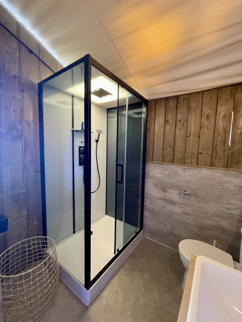 Modern bathroom inside safari tent Luna Lodge at Camping de Noetselerberg with glass shower and wood walls.