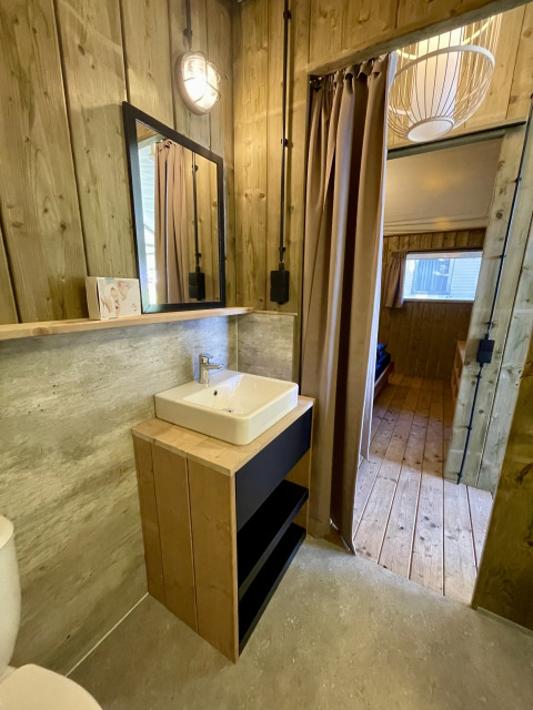 Baño con paredes de madera, lavabo y espejo en una tienda safari, Luna Lodge, Camping the Noetselerberg.