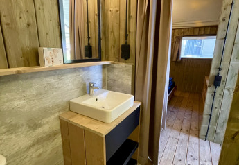 Baño con paredes de madera, lavabo y espejo en una tienda safari, Luna Lodge, Camping the Noetselerberg.