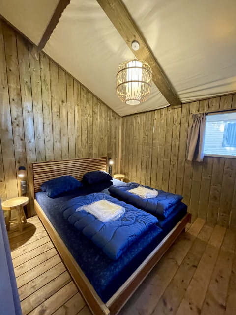 Bedroom inside Luna Lodge safari tent at Camping the Noetselerberg in the Netherlands, with wooden decor.