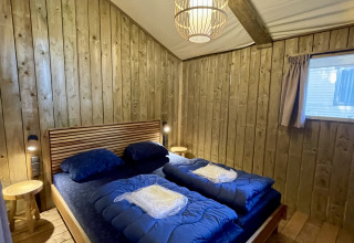 Slaapkamer in Luna Lodge safaritent op Camping the Noetselerberg, Nederland, met houten wanden en bed.