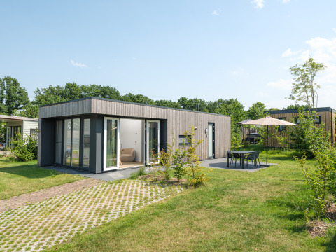 Moderne Oak Lodge mit großen Fenstern, Terrasse, Gartenmöbeln und Sonnenschirm an einem sonnigen Tag.
