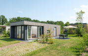 Moderna Oak lodge con ampie finestre, patio e mobili da giardino sotto ombrellone in una giornata di sole.