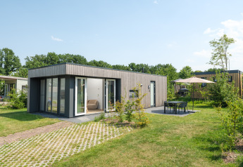 Moderne Oak Lodge mit großen Fenstern, Terrasse, Gartenmöbeln und Sonnenschirm an einem sonnigen Tag.