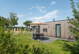 Moderne træhytte med terrasse, havemøbler og parasol på Vakantiepark Hölte i Holland under blå himmel.
